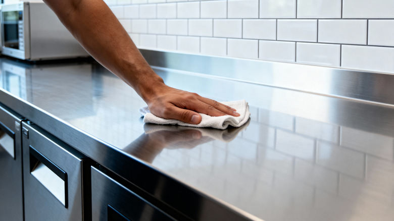 A person is cleaning a shiny stainless steel surface with a white clot