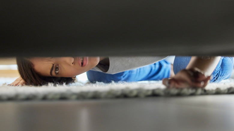 A woman looking under a couch for mold