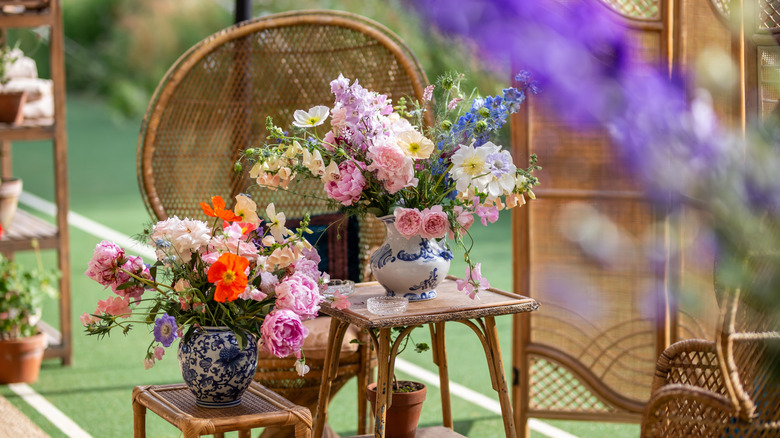 Two vases with eclectic mixed blooms on wicker furniture outdoors.