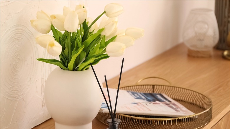 Console table with white tulips in a white vase, oil diffuser, and magazine tray.