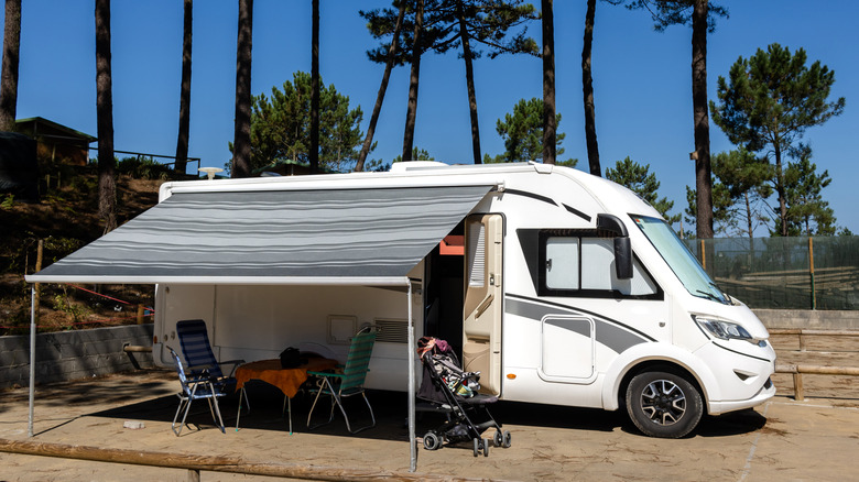 An motorhome parked at an RV park with chairs and stroller in front
