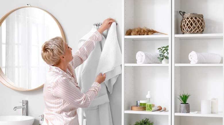 Woman hanging towel from hook in bathroom.