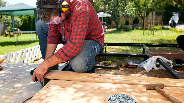 Person wearing ear protection works on a wooden fence on the ground