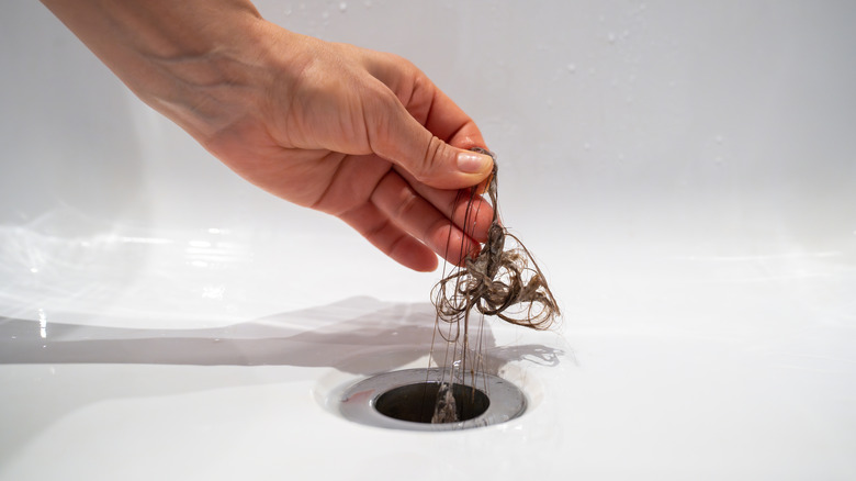 Woman pulls hair clog out of drain with bare hand.