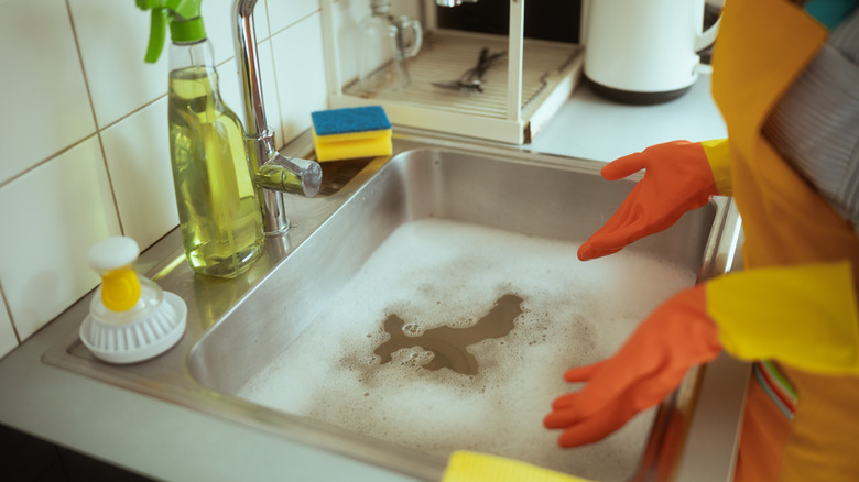 Person wearing rubber gloves standing in front of clogged kitchen sink