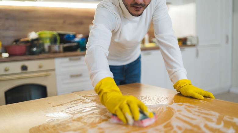 A man cleaning a wood-look table with a soapy solution