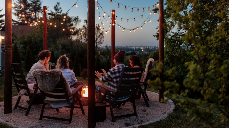 People enjoying a fire pit together at dusk in a residential backyard with a view over a city.