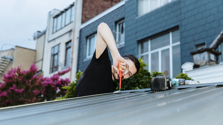 Person tightening screws on a shed roof with an orange screwdriver