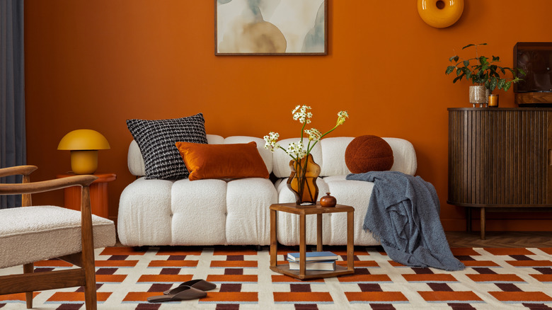 A living room with orange walls, a patterned rug, and printed throw pillows.