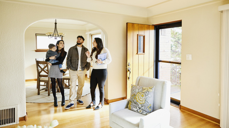 A real estate agent giving a tour talks to a young family in a neutral living room