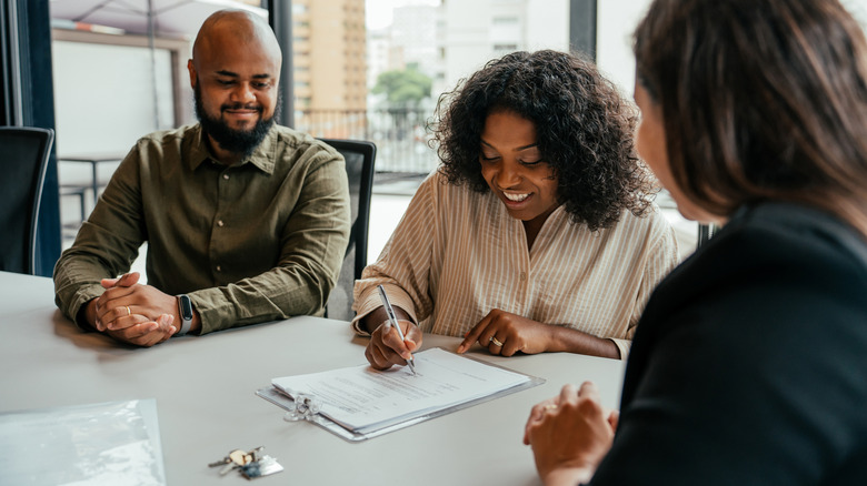 An excited couple sits with a mortgage broker while signing a real estate contract