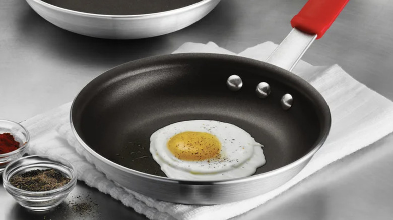 The Tramontina 8-inch fry pan on a countertop with a fried egg inside and spices to the side of the pan