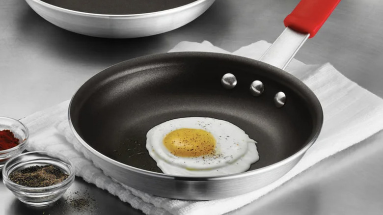 The Tramontina 8-inch fry pan on a countertop with a fried egg inside and spices to the side of the pan