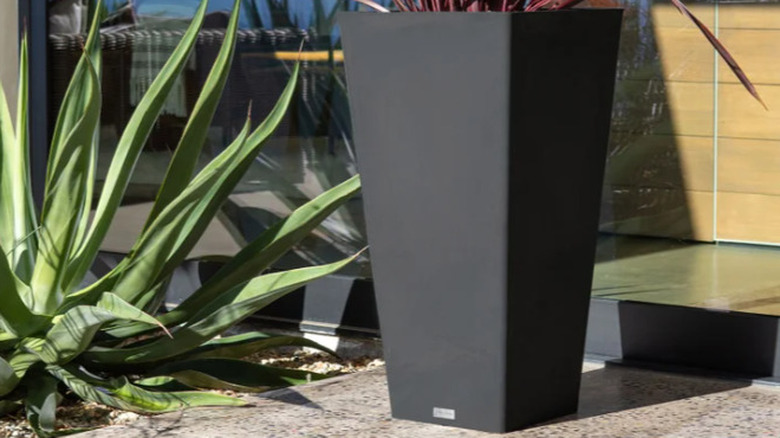 A Veradek 26-inch Taper Planter outside on a patio next to a plant