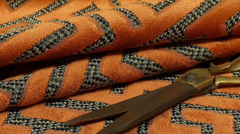 Closeup of orange cut velvet fabric with scissors resting on top.