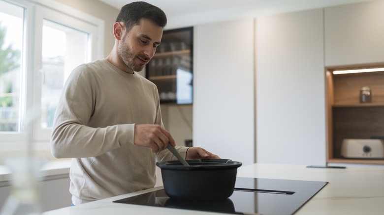 A man in a beige shirt cooking on an induction cooktop