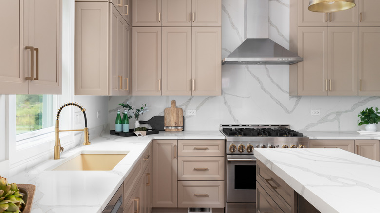 A kitchen with white counters and light brown upper and lower cabinets and an island