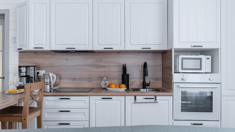 A kitchen with more of a classic feel with a simple wooden backsplash and counter and painted wooden white cabinets
