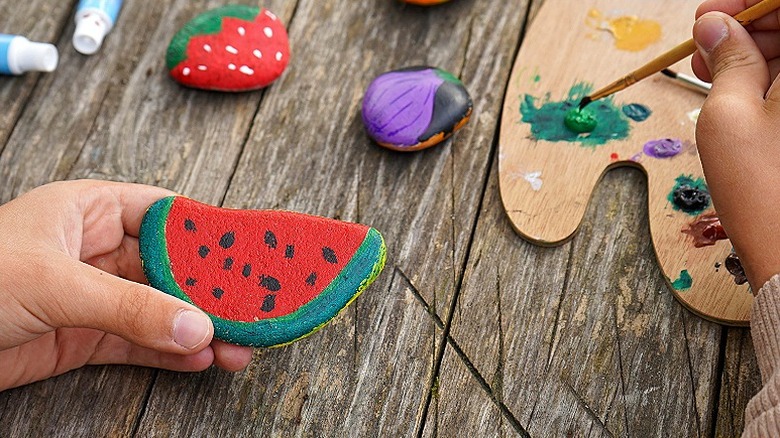 Close-up of a person using a paintbrush to paint a rock that looks like a watermelon