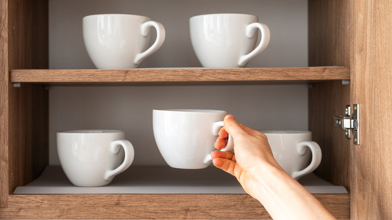 A hand grabbing a mug from an organized shelf of mugs.
