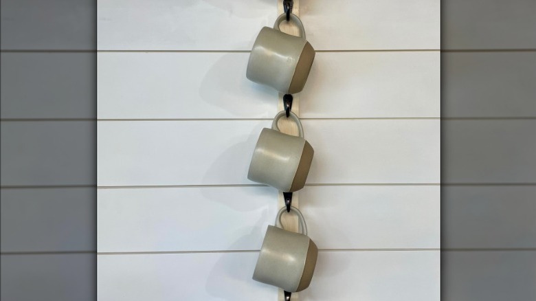 Mugs hanging from vertical wall-mounted rack.