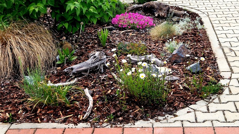 A mulched garden bed next to a brick driveway with some of the mulch spilling out