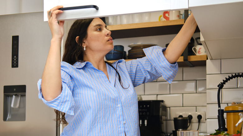 Woman opens a deep kitchen cabinet, looking for plates.