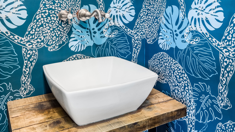 A white vessel sink in a powder room covered in a blue cheetah-print wallpaper.