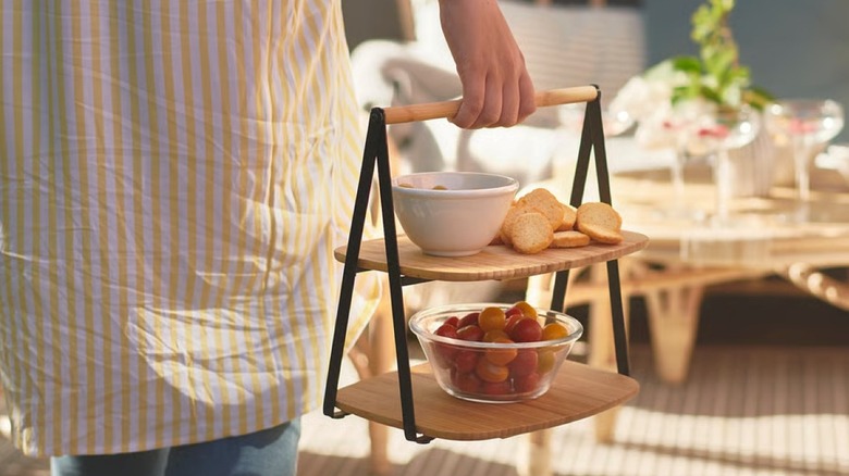 A person carrying a two-tiered wooden tray with slices of bread and tomatoes on it