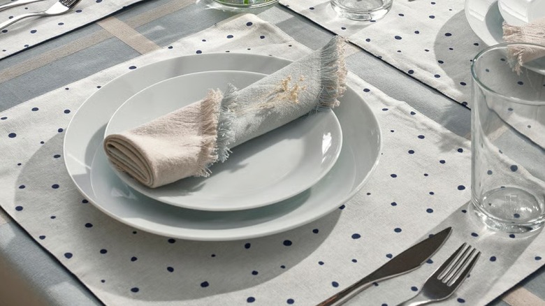 A polka dot jute placemat under a table setting with a rolled napkin