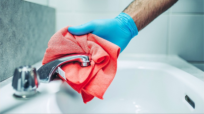 Gloved hand cleaning bathroom sink