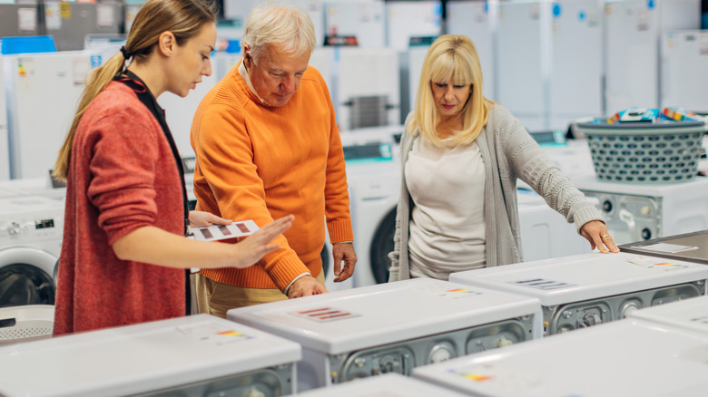 A female salesperson is advising a senior couple on washing machines