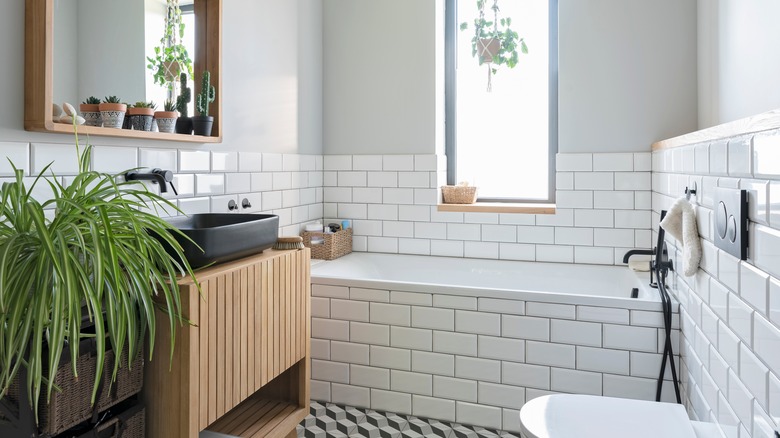 Modern bathroom in industrial design in stylish interior. White tiles, wooden cabinet and mirror and bathroom sink in black colour in new apartment.