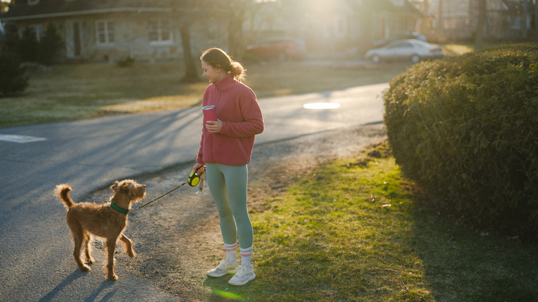 A person stands in a front yard while smiling at her dog