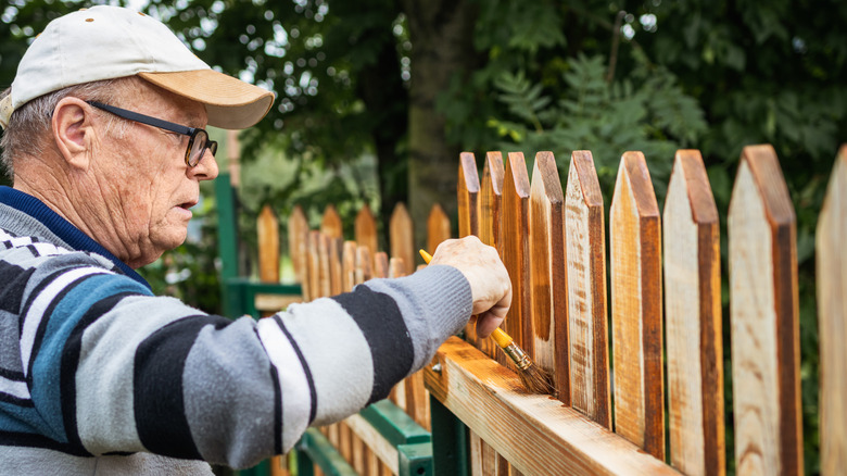 A man painting a fence at the edge of a property