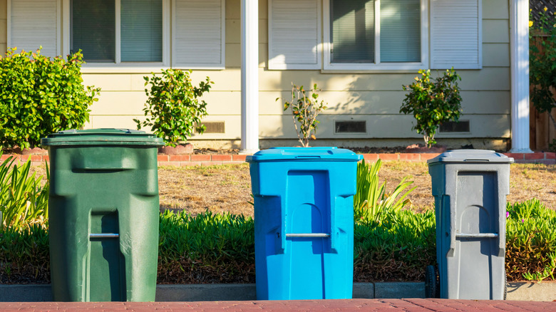 Wheeled compost, recycling, and trash cans set outside of a home on a residential curb for city pickup.