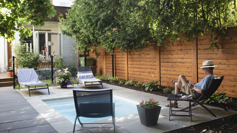 Man reads near small pool with fence beside.