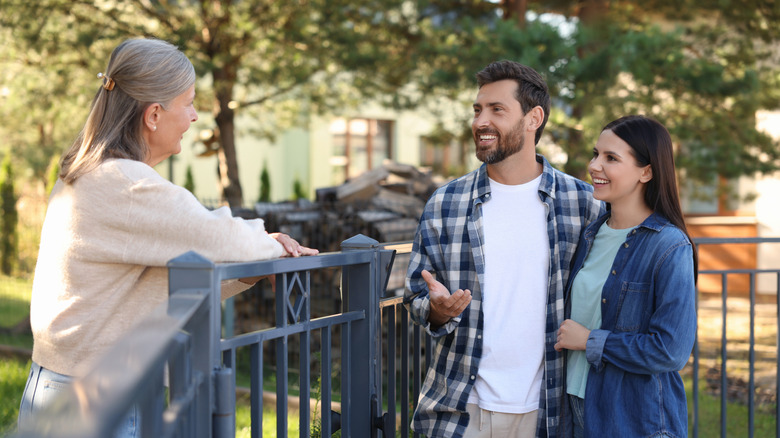 Happy young couple talking to senior woman near fence outdoors.