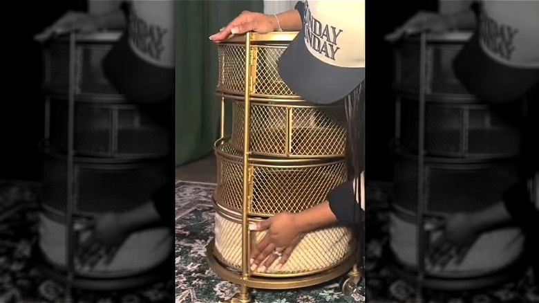 Person touching gold metal tiered storage cart with a blanket in the bottom shelf