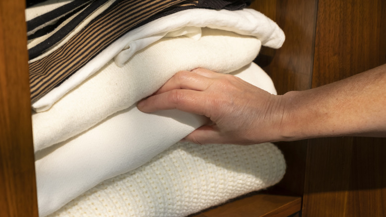 A hand reaching towards folded blankets.