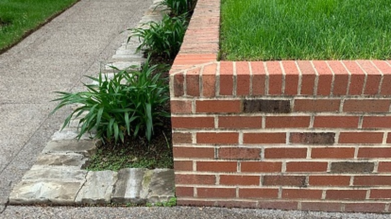 A red brick retaining wall on the corner of a front yard next to a sidewalk in a residential neighborhood.