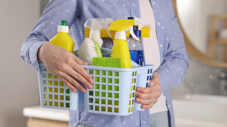 A person carrying a basket of cleaning supplies