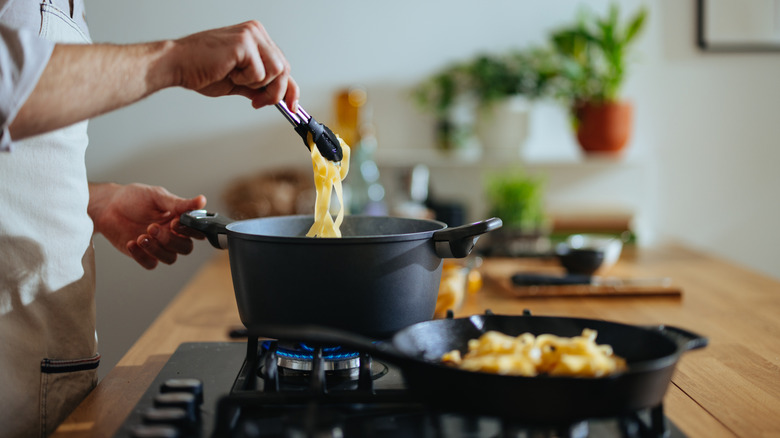 A person cooking pasta in a black pot on a gas stove