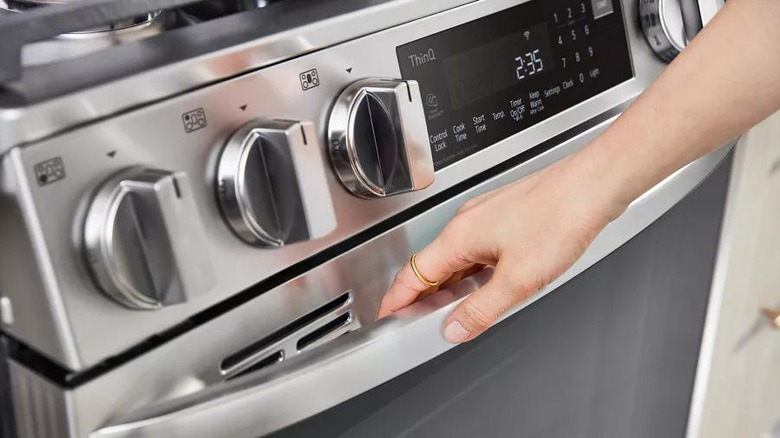 A hand reaching for the oven handle of the LG LSDL6336F
