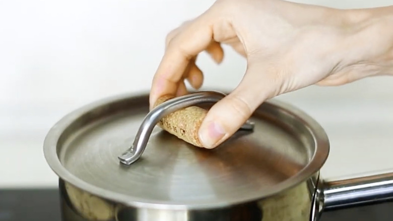 Person picking up a hot metal pod lid with a wine cork underneath the handle