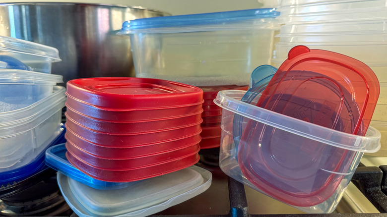 Stacks of mismatched reusable plastic food storage containers and lids in a kitchen cabinet.