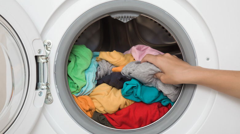 A person adds clothing to a front load washer that is filled just past the halfway point