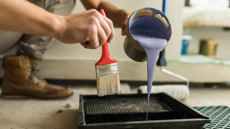 Person holding paint brush and pouring paint into a pan for a home renovation
