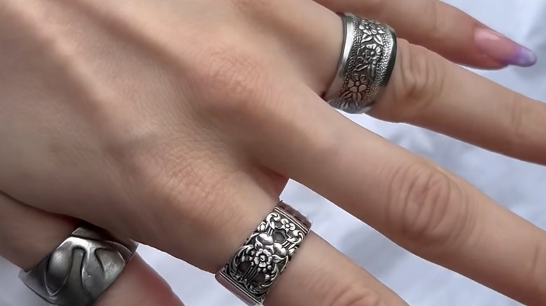 A hand adorned with rings made from thrifted silver spoons.