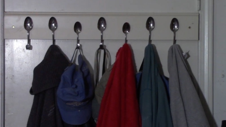 Coats hang on hooks made from bent spoons attached to a wall mounted rack.